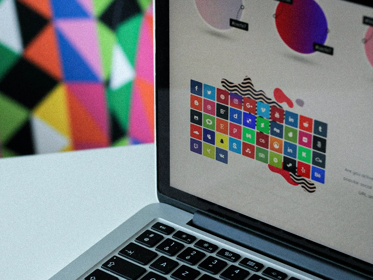 Social media logo icons in a grid on a laptop screen, colorful geometric pattern on the wall in the out of focus background.